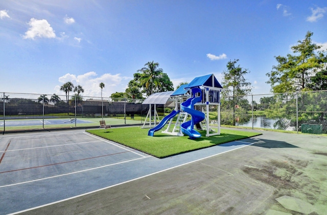 view of play area with a water view, tennis court, and a lawn