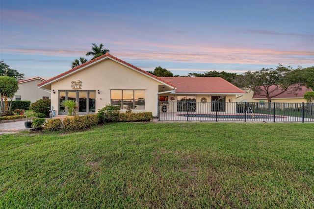 rear view of house featuring a fenced in pool, a tile roof, stucco siding, a lawn, and fence