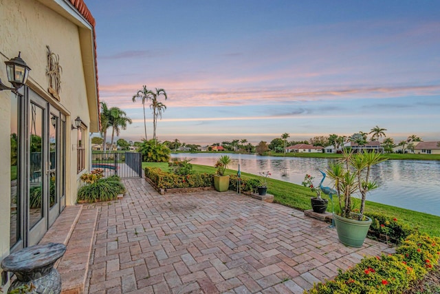 patio terrace at dusk featuring a water view and a gate