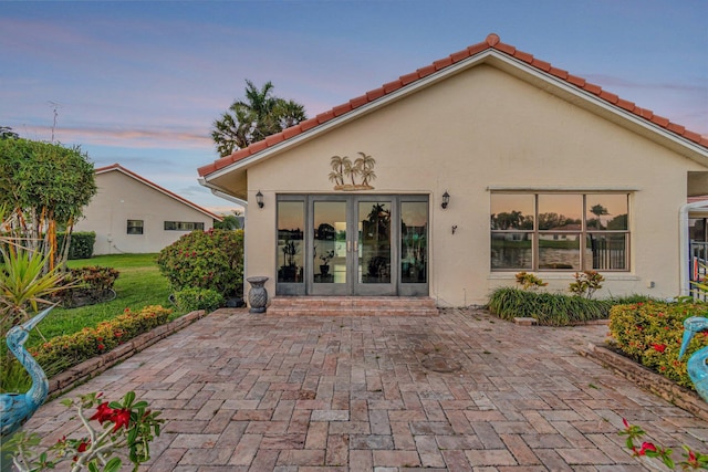 rear view of house featuring a patio, french doors, a tiled roof, and stucco siding