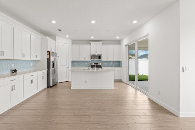 kitchen featuring a kitchen island with sink, light hardwood / wood-style floors, white cabinets, and appliances with stainless steel finishes