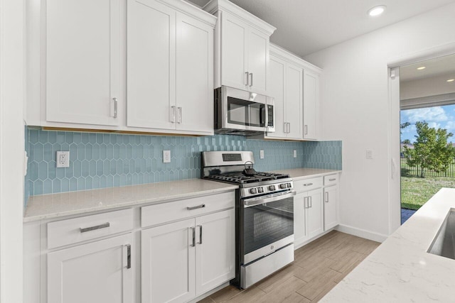 kitchen featuring appliances with stainless steel finishes, light stone counters, tasteful backsplash, white cabinets, and light wood-type flooring