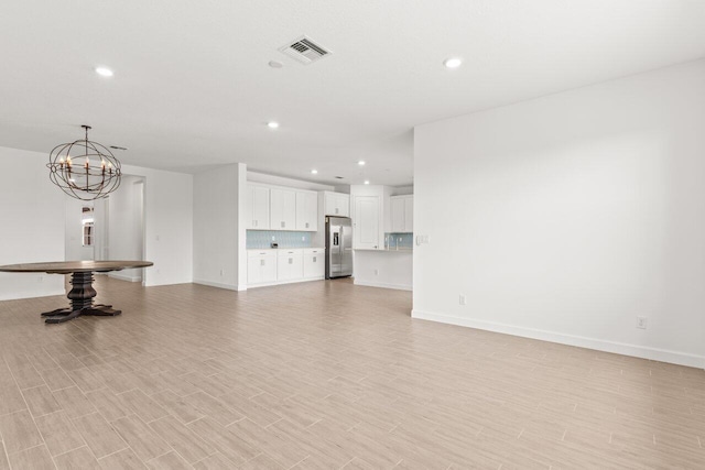 unfurnished living room featuring a notable chandelier and light hardwood / wood-style floors