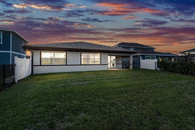 back house at dusk featuring a lawn