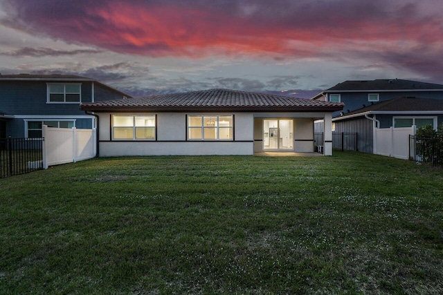 back house at dusk with a lawn and a patio area