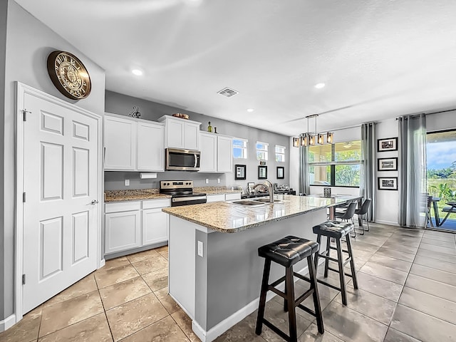 kitchen with stainless steel appliances, an island with sink, sink, and white cabinets