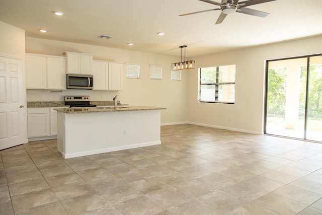 kitchen featuring appliances with stainless steel finishes, an island with sink, white cabinets, hanging light fixtures, and light stone counters