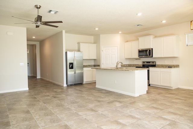 kitchen featuring sink, white cabinets, stainless steel appliances, light stone countertops, and a center island with sink