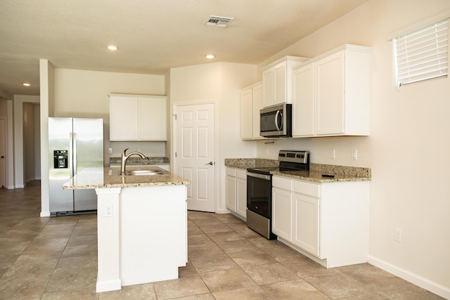 kitchen with sink, appliances with stainless steel finishes, a kitchen island with sink, white cabinetry, and light stone counters