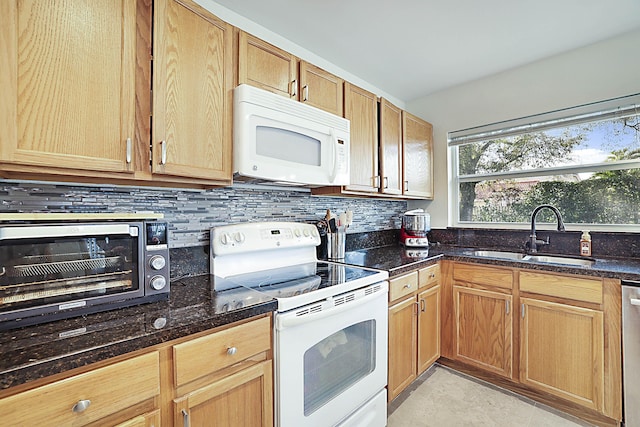 kitchen featuring sink, white appliances, dark stone counters, and decorative backsplash