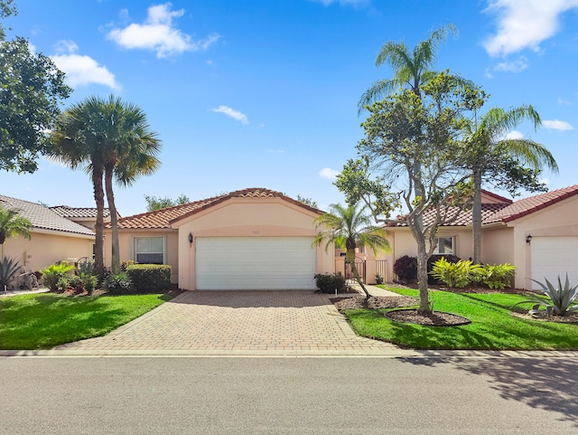 mediterranean / spanish house featuring a garage, a tile roof, decorative driveway, a front lawn, and stucco siding