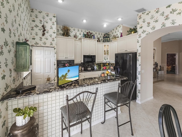 kitchen featuring light tile patterned floors, black appliances, white cabinets, kitchen peninsula, and dark stone counters