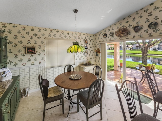 dining room featuring lofted ceiling, light tile patterned flooring, a textured ceiling, and a water view