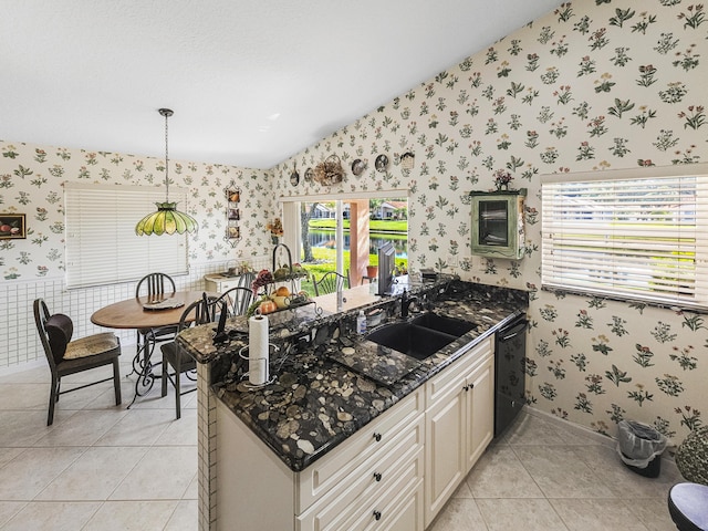 kitchen with pendant lighting, dishwasher, lofted ceiling, sink, and dark stone counters