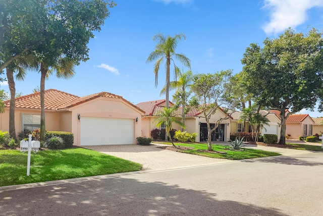 mediterranean / spanish-style house with stucco siding, a tile roof, an attached garage, decorative driveway, and a front yard