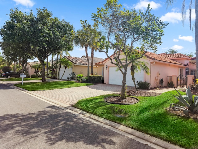 mediterranean / spanish-style home featuring a garage, stucco siding, a tile roof, decorative driveway, and a front yard