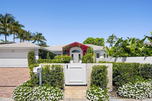 view of front of house with a gate, an attached garage, a fenced front yard, a tile roof, and decorative driveway