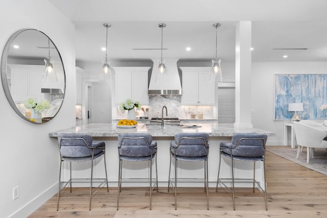 kitchen with light stone counters, hanging light fixtures, custom range hood, and white cabinets