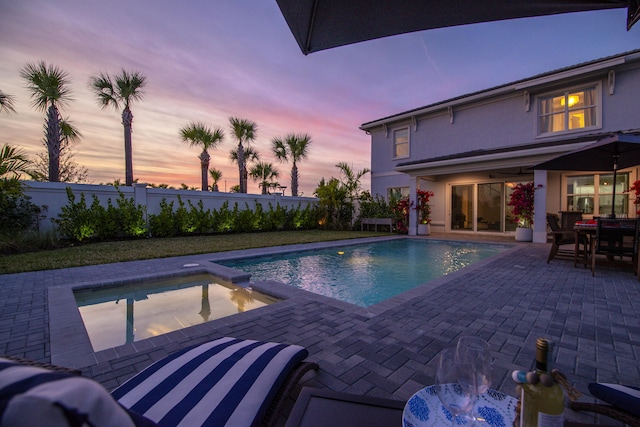 pool at dusk featuring an in ground hot tub and a patio area