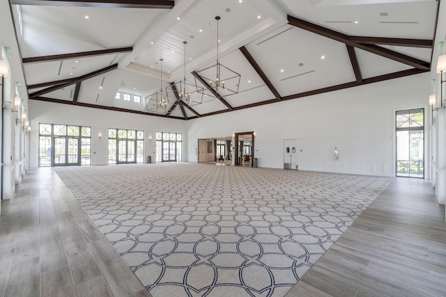 unfurnished living room featuring beam ceiling, high vaulted ceiling, light hardwood / wood-style floors, and a chandelier