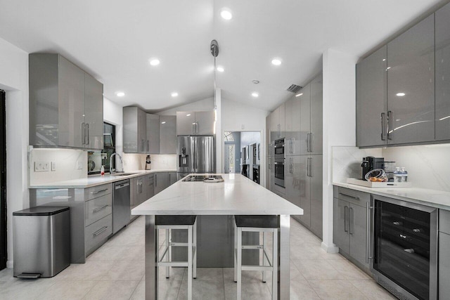 kitchen with gray cabinets, a kitchen bar, stainless steel appliances, a kitchen island, and beverage cooler