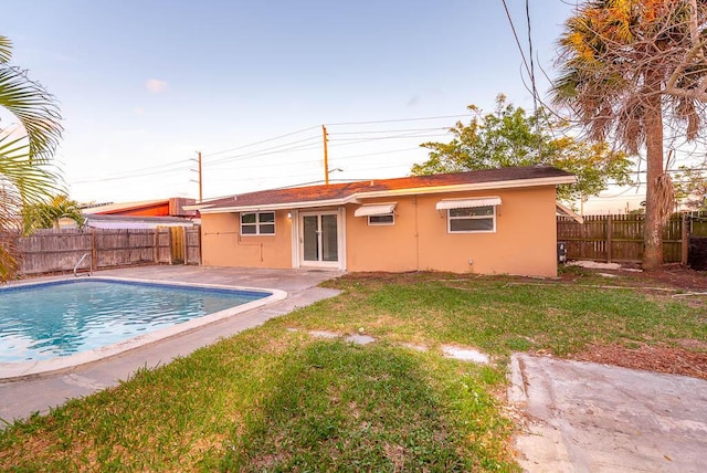 rear view of house featuring a wall mounted AC, a patio, a fenced in pool, and a lawn