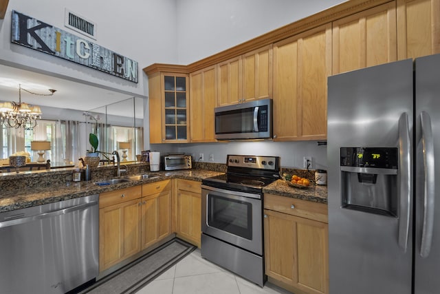 kitchen featuring appliances with stainless steel finishes, sink, dark stone countertops, hanging light fixtures, and light tile patterned floors