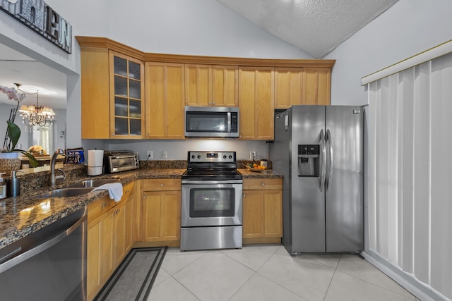 kitchen with vaulted ceiling, appliances with stainless steel finishes, light tile patterned floors, and dark stone counters