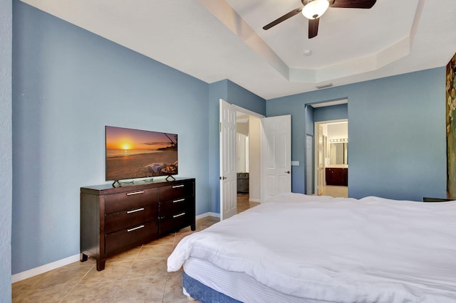 bedroom with a tray ceiling, ensuite bath, baseboards, and light tile patterned floors