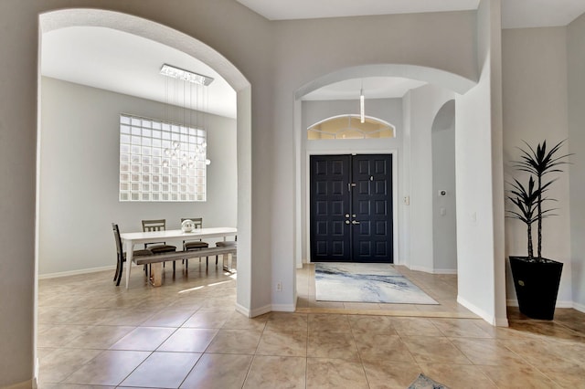 entrance foyer featuring arched walkways, light tile patterned flooring, and baseboards