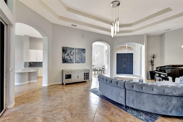 living area with light tile patterned floors, visible vents, arched walkways, a high ceiling, and a tray ceiling