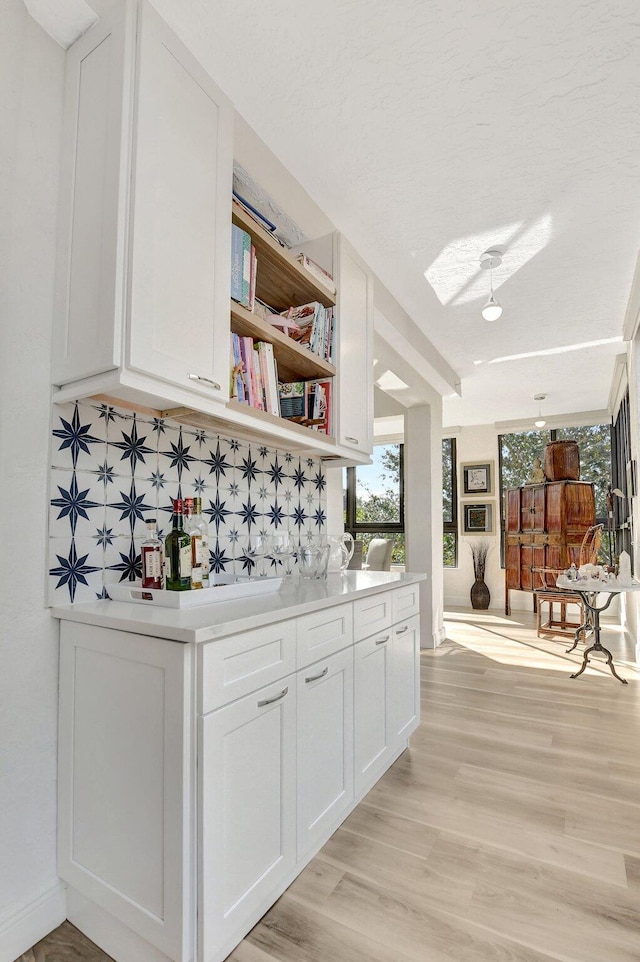 bar with light wood-type flooring, decorative backsplash, and white cabinets