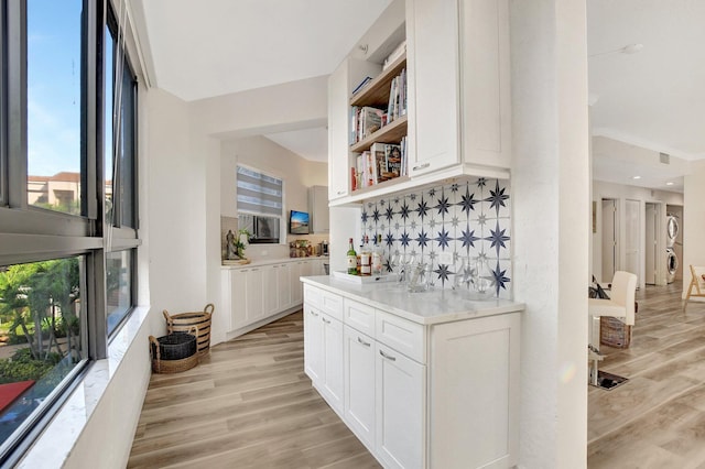 bar featuring white cabinetry, stacked washing maching and dryer, and light hardwood / wood-style floors