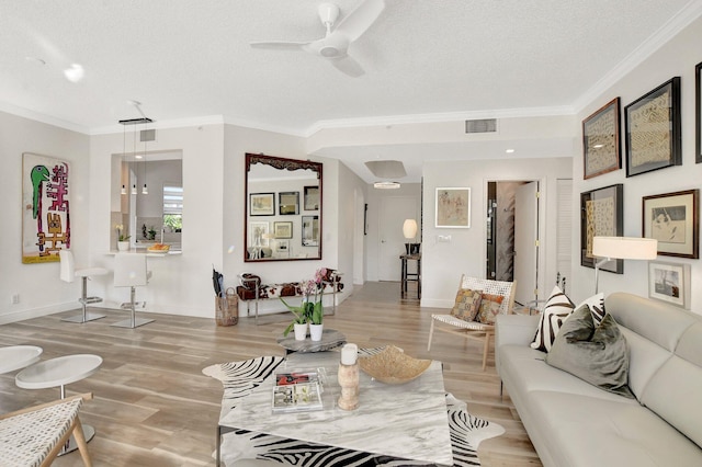 living room with ceiling fan, ornamental molding, a textured ceiling, and light wood-type flooring