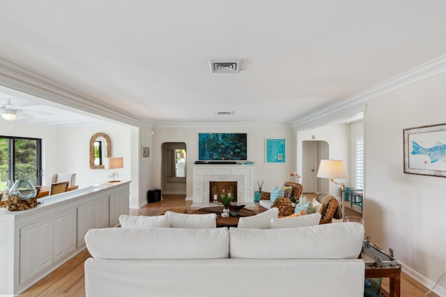 living room featuring a premium fireplace, ornamental molding, and light wood-type flooring