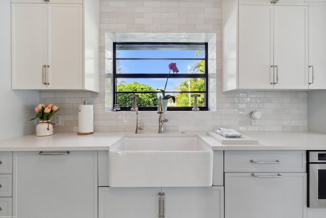 kitchen with white cabinetry, sink, stainless steel oven, and decorative backsplash