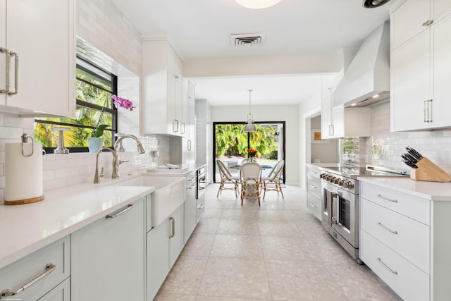 kitchen with pendant lighting, sink, white cabinets, custom exhaust hood, and stainless steel range