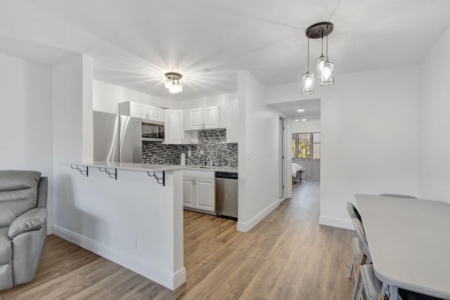 kitchen with white cabinetry, hanging light fixtures, stainless steel appliances, light hardwood / wood-style floors, and kitchen peninsula