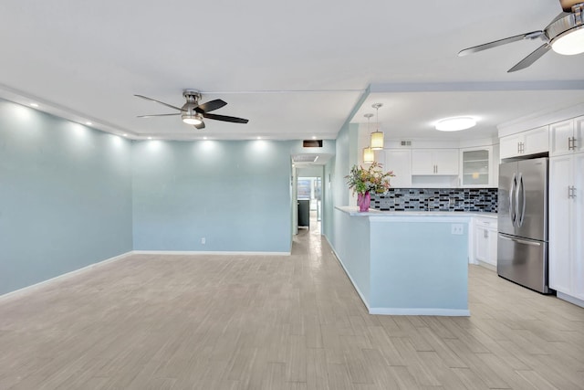 kitchen featuring light wood finished floors, backsplash, freestanding refrigerator, white cabinets, and ceiling fan