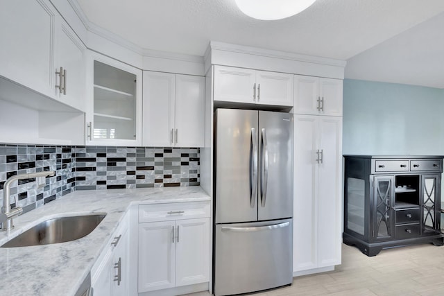 kitchen featuring decorative backsplash, glass insert cabinets, freestanding refrigerator, white cabinetry, and a sink