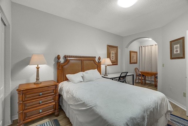 bedroom featuring baseboards, arched walkways, wood finished floors, and a textured ceiling