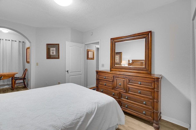 bedroom featuring arched walkways, light wood-style floors, baseboards, and a textured ceiling