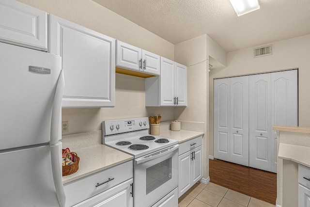 kitchen with white appliances, white cabinetry, visible vents, light tile patterned flooring, and light countertops