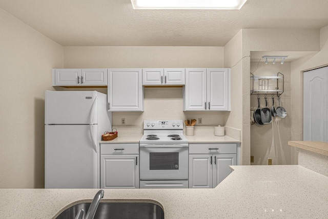 kitchen featuring rail lighting, white appliances, white cabinets, and a sink