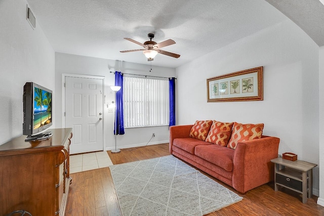 living area with baseboards, a textured ceiling, visible vents, ceiling fan, and wood finished floors