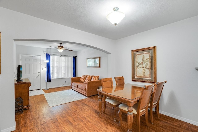 dining area featuring baseboards, a ceiling fan, arched walkways, and wood finished floors