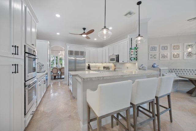 kitchen featuring a breakfast bar area, white cabinetry, tasteful backsplash, decorative light fixtures, and kitchen peninsula