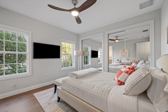 bedroom with multiple windows, two closets, wood-type flooring, and ceiling fan