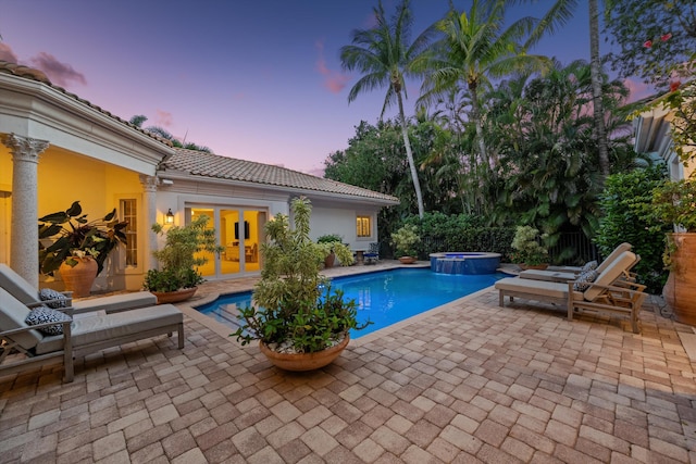 pool at dusk with a patio area, french doors, and an in ground hot tub