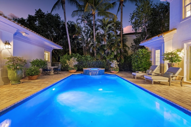 pool at dusk with a patio and an in ground hot tub